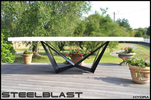 Table moderne avec plateau béton ciré blanc et base en acier métal noir.